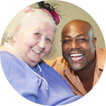 Smiling man and woman, she is wearing a lavender shirt and festive pink hat